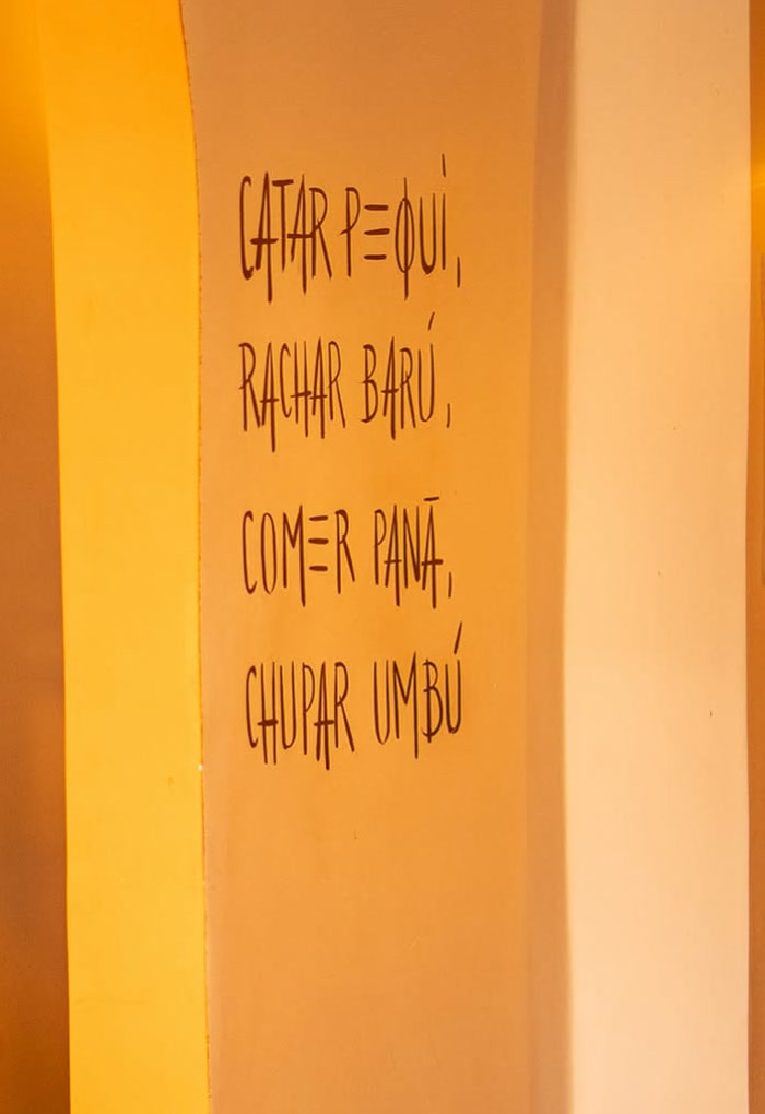 Frase pintada à mão na coluna do salão: catar pequi, rachar baru, comer panã, chupar umbu.