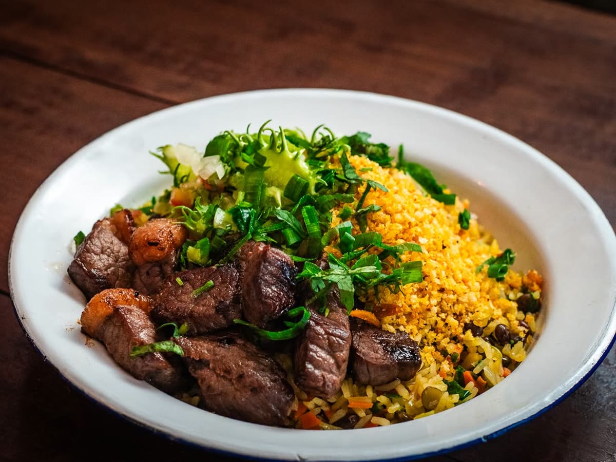 Andu de dois: carne de sol, farofa de pequi, vinagrete de maxixe e arroz com feijão-andu, no prato esmaltado de borda azul.