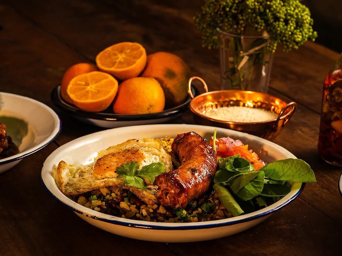 Andu de dois na versão com linguiça frita, ovo e salada, na mesa posta com laranjas e panela de cobre.