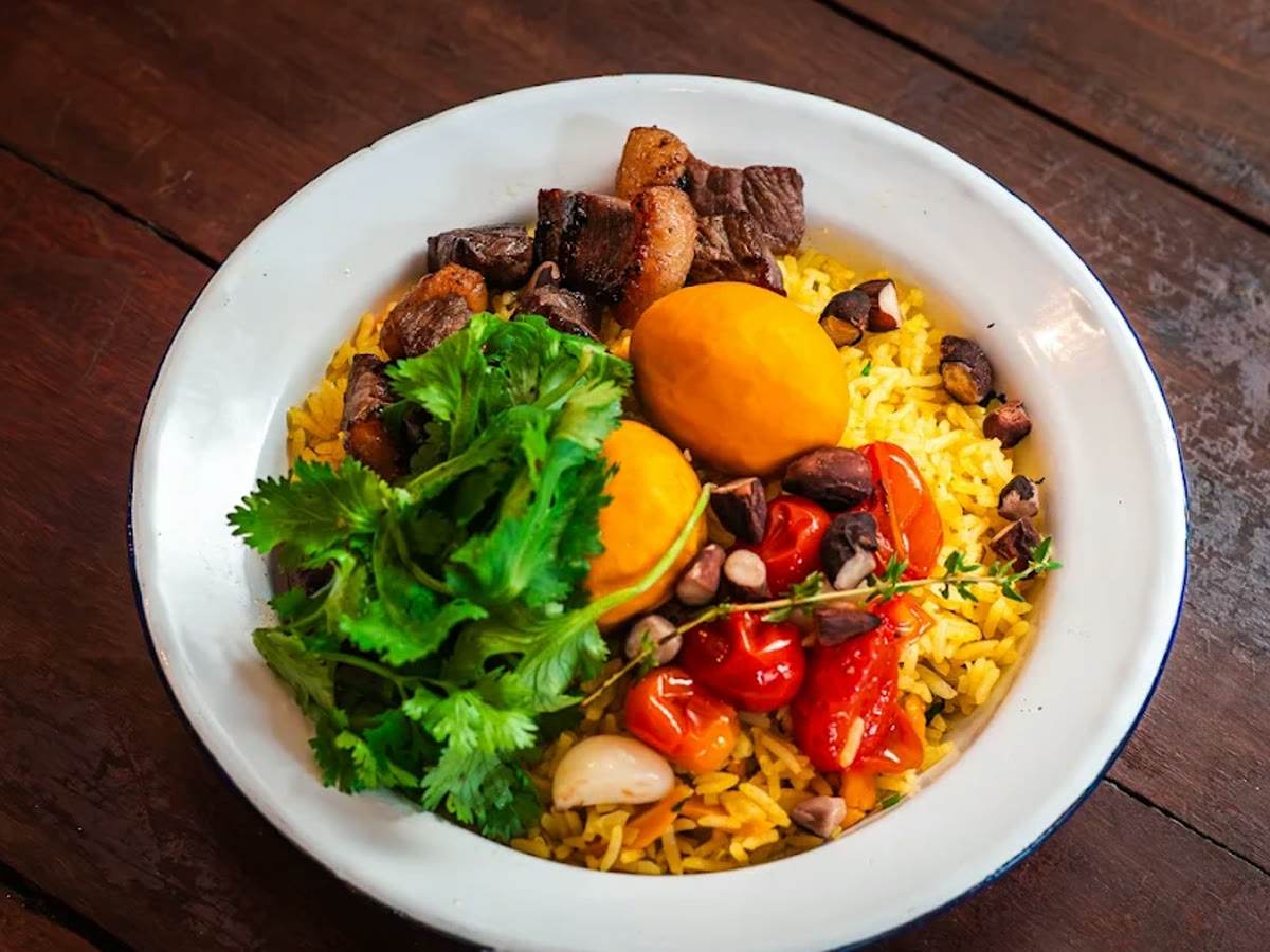 Arroz com pequi servido no prato esmaltado de borda azul, sobre a mesa de madeira escura.