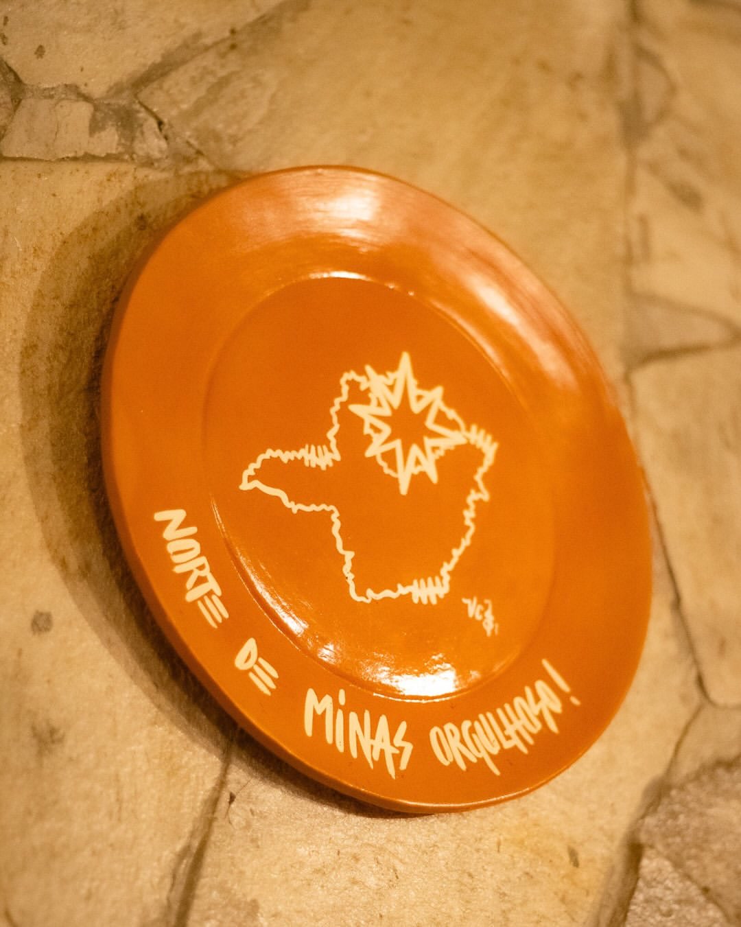 Louça de barro pendurada na parede de pedra, com o mapa de Minas, uma estrela marcando o Norte e a frase pintada à mão: Norte de Minas orgulhoso.